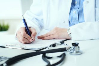 Mid section of female doctor writing prescription to patient at worktable.